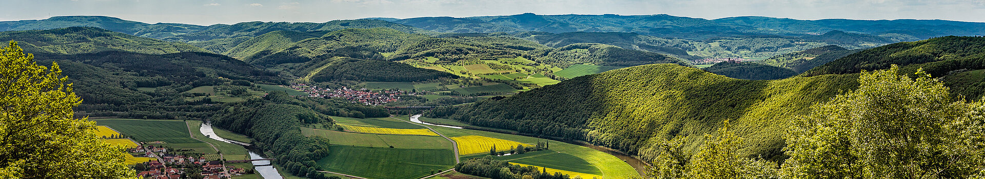 Ausblick von der Teufelskanzel auf das Werratal. Links und Rechts ragt das grüne Mittelgebirge in die Höhe. In der Mitte fließt der Fluss, Werra, im Tal entlang.