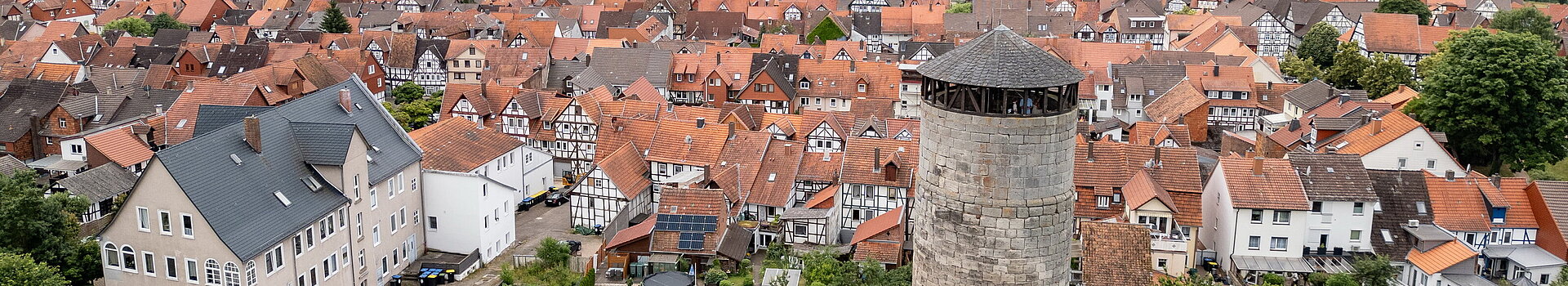 Alter Turm mit Stadtmauer von oben. Hinter der Stadtmauer reihen sich die Fachwerkhäuser aneinander.
