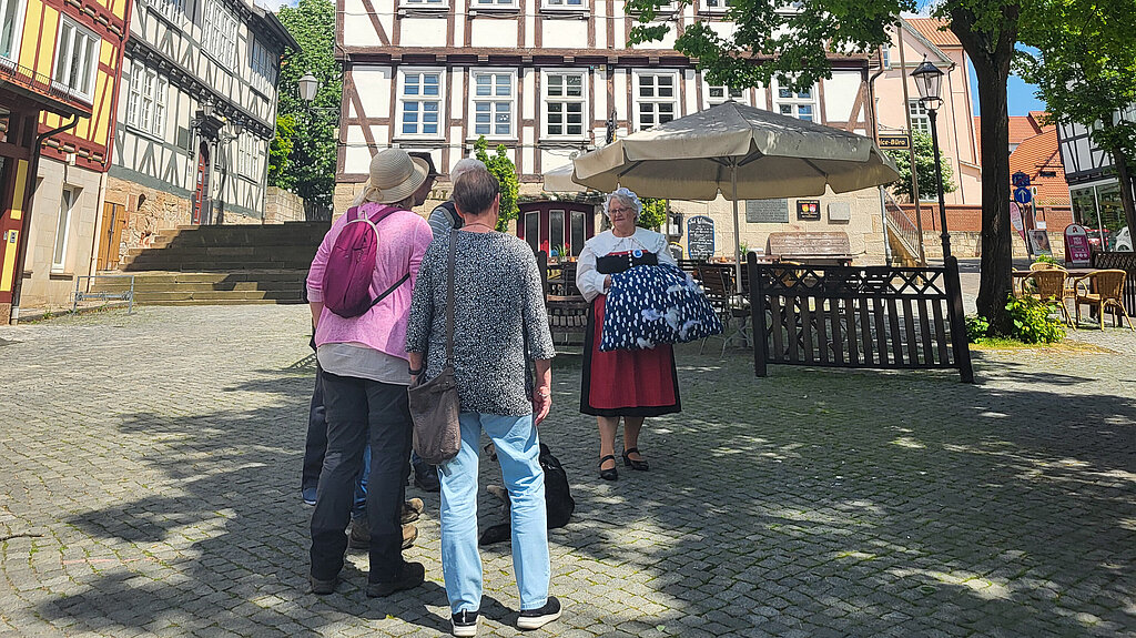 Eine ältere Frau als Frau Holle verkleidet erzählt einer Gruppe Erwachsener die Stadtgeschichte.
